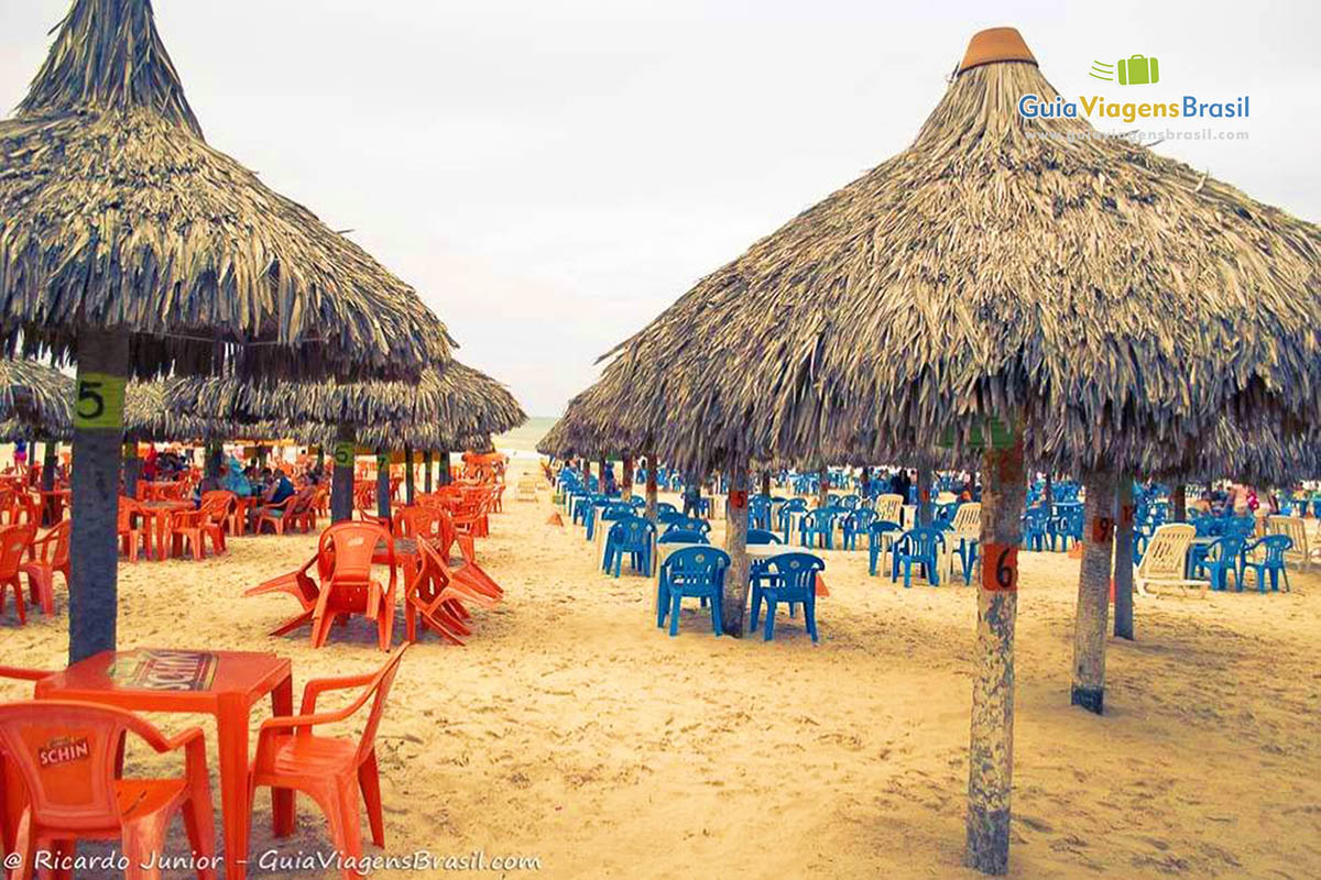 Imagem de guarda sol de sapê com mesas e cadeiras para turistas.